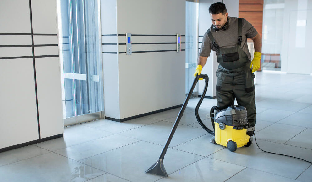Professional janitorial service worker using a wet vacuum cleaner on an office building tiled floor