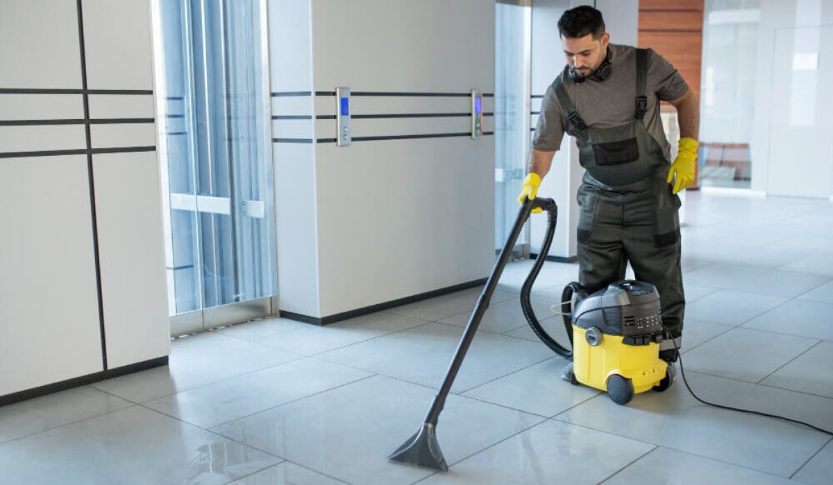 Professional janitorial service worker using a wet vacuum cleaner on an office building tiled floor